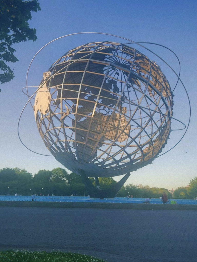 Flushing Meadows Park in Queens, which has a large plaza surrounded by trees, with a building-sized metal globe in the middle. The globe has metal continents, latitude and longitude lines, and a few circular rings around the globe in overlapping orbits.